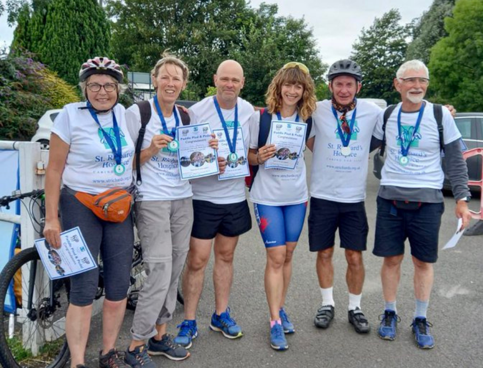 A group of men and women wearing t shirts with the hospice logo and medals, holding certificates.