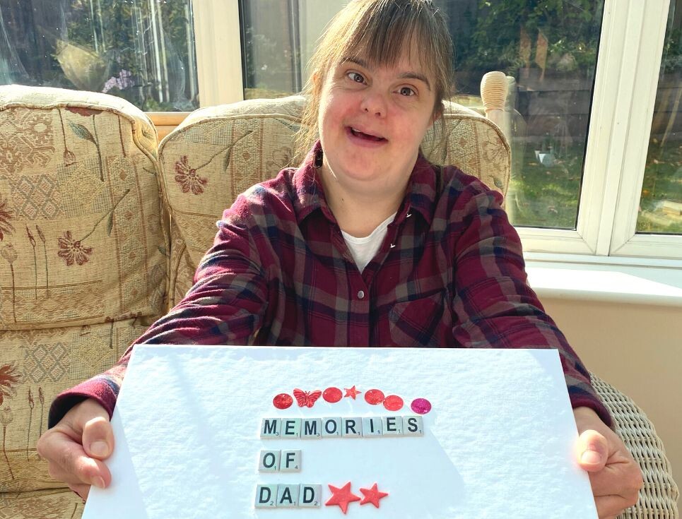Jen smiles holding her memory box. The box is decorated with lettering which reads Memories of Dad.