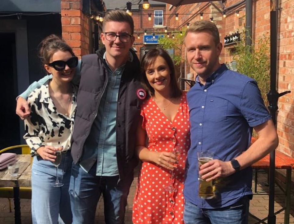 A group of people stand together in the sunshine.