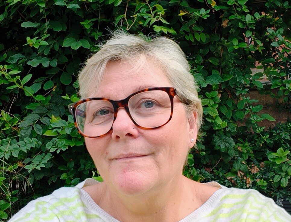 Alyson pictured in front of a dark green, leafy hedge. She is wearing a light green and white stripy jumper.