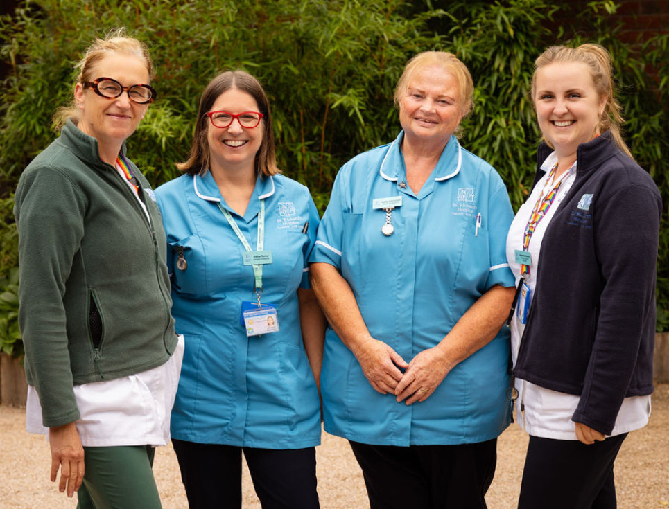 Four members of the St Richard's Living Well Team stand side-by-side in the hospice's courtyard garden. Everyone is smiling.