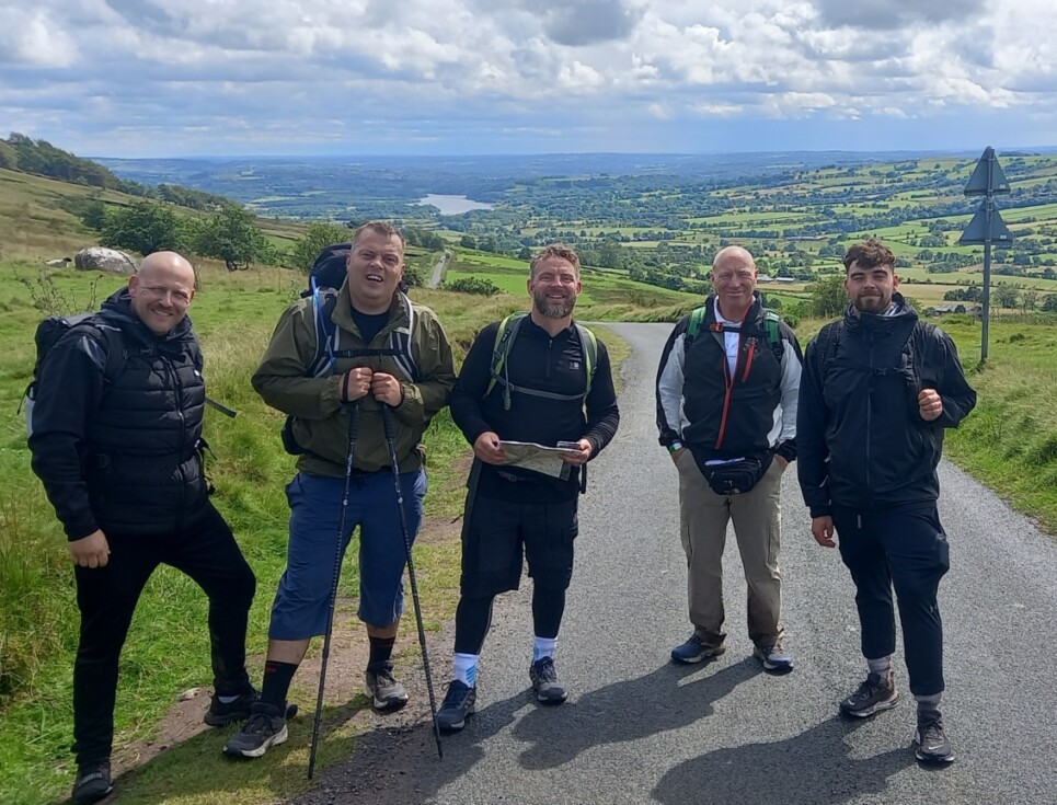 Five people standing on a road with countryside all around