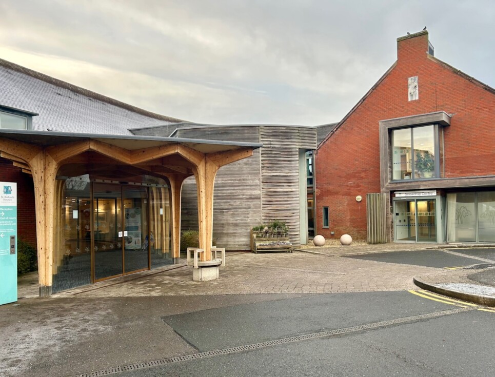 Building with wooden canoped entrance and vertical hospice sign.